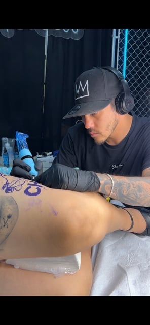 Tattoo artist wearing black cap and gloves performing a tattoo on a clients arm in a studio setting