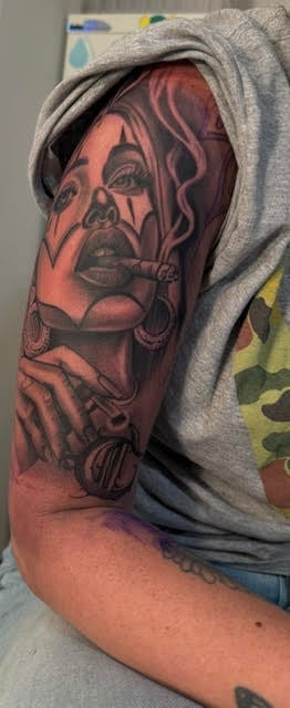 Red and black portrait tattoo on a persons arm featuring a stylized face with decorative elements